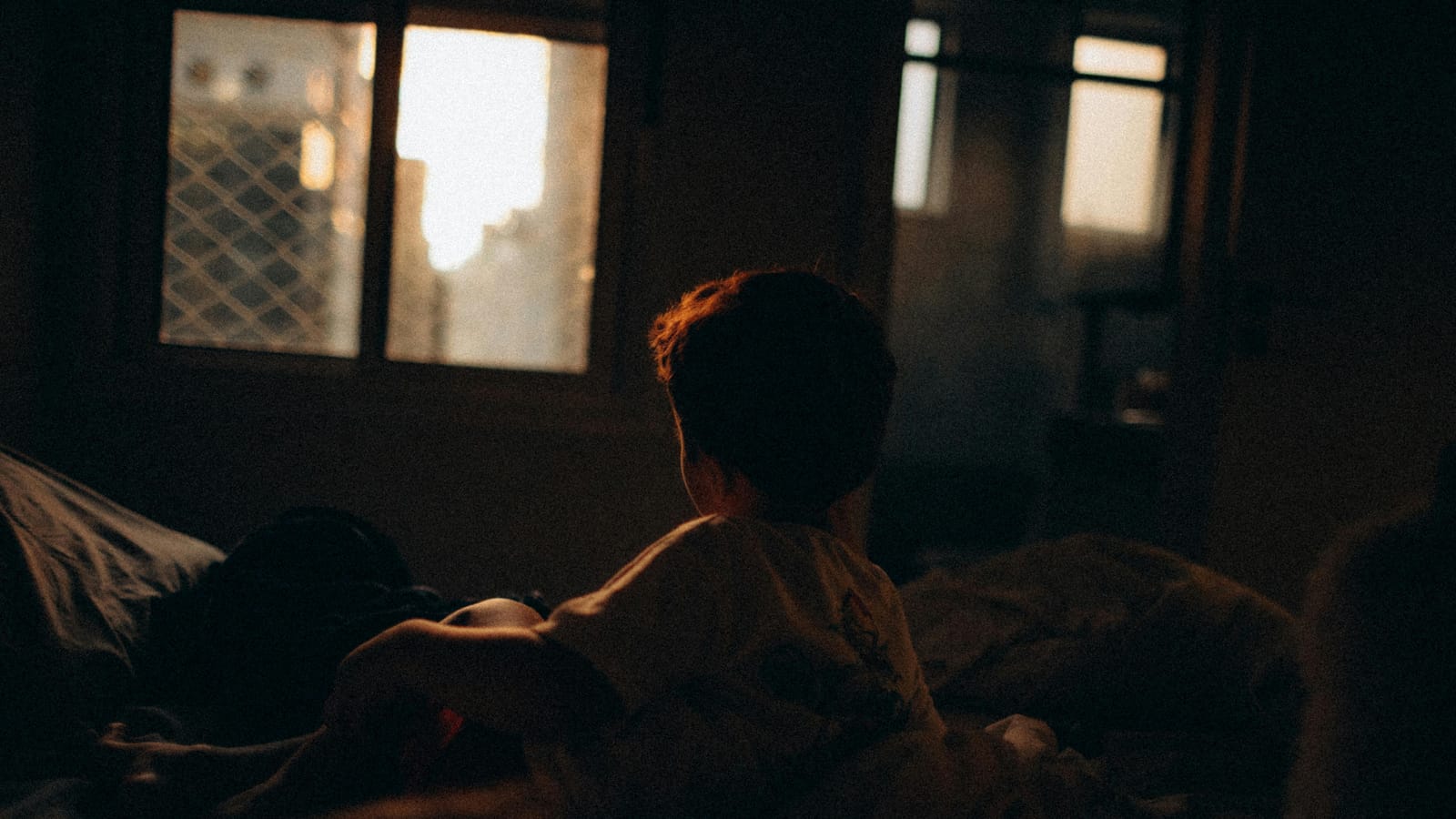A contemplative child looking through a window as the sun sets, creating a warm atmosphere.