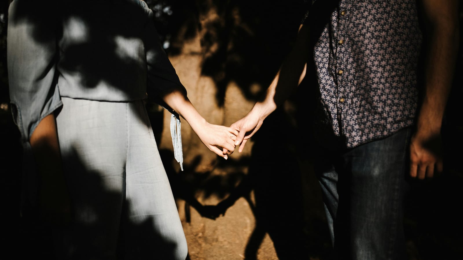 Romantic couple holding hands, capturing intimate shadows and sunlight outdoors.