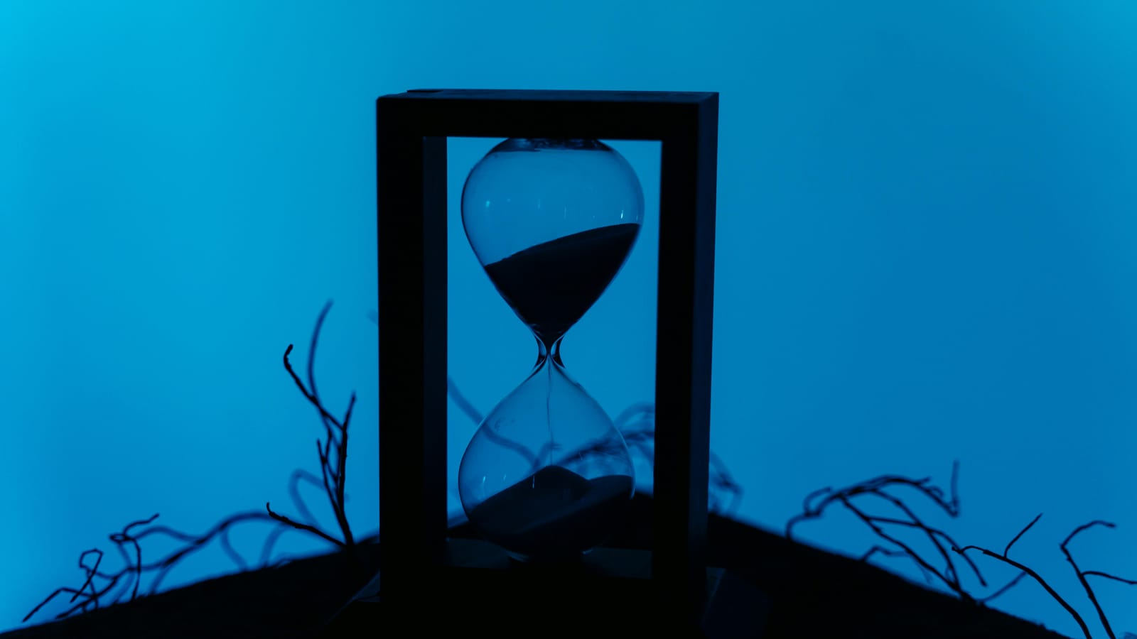 A silhouette of an hourglass set against a vivid blue background, highlighting the passage of time.