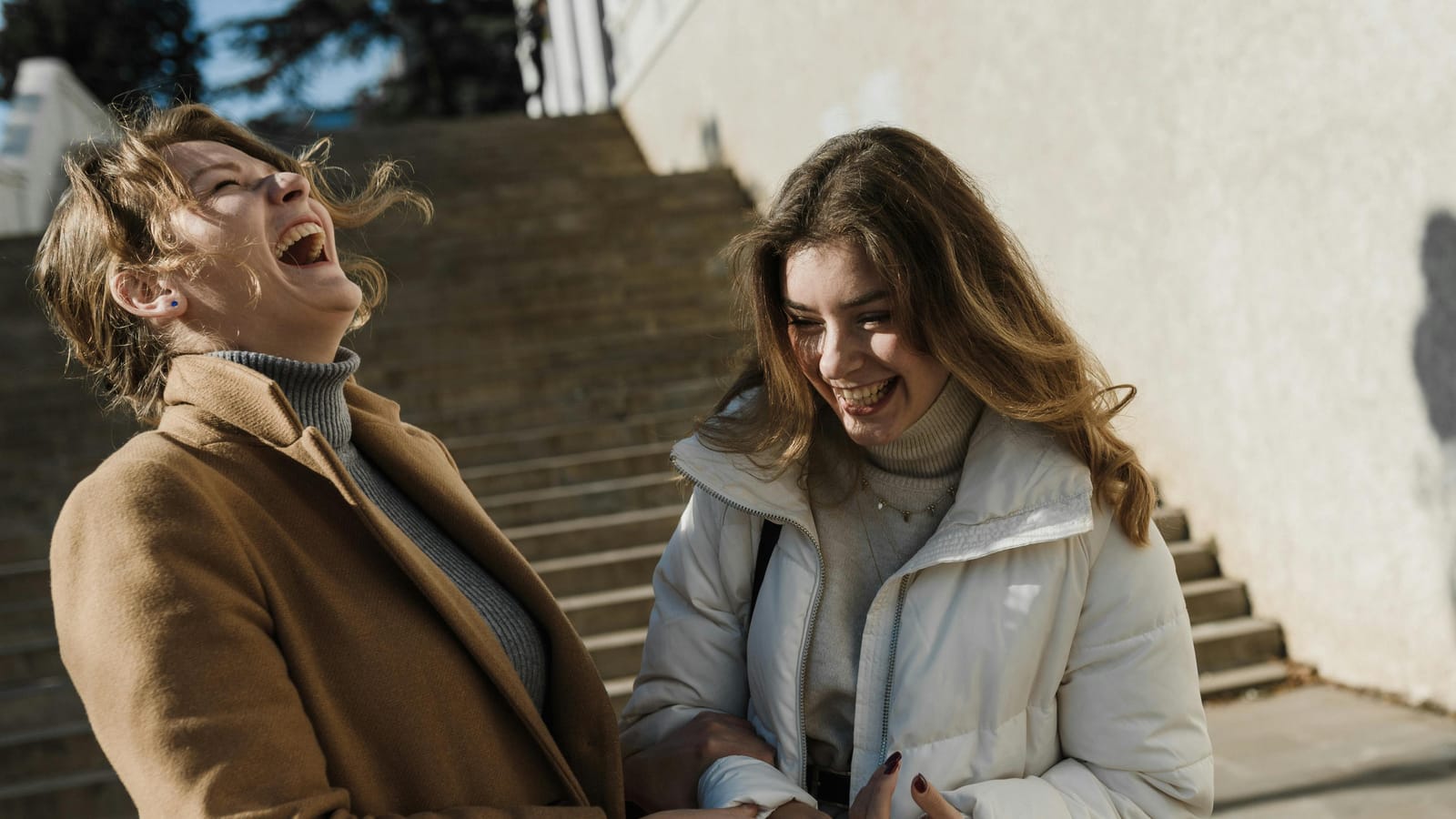 Two young women laughing together outside on a sunny day.