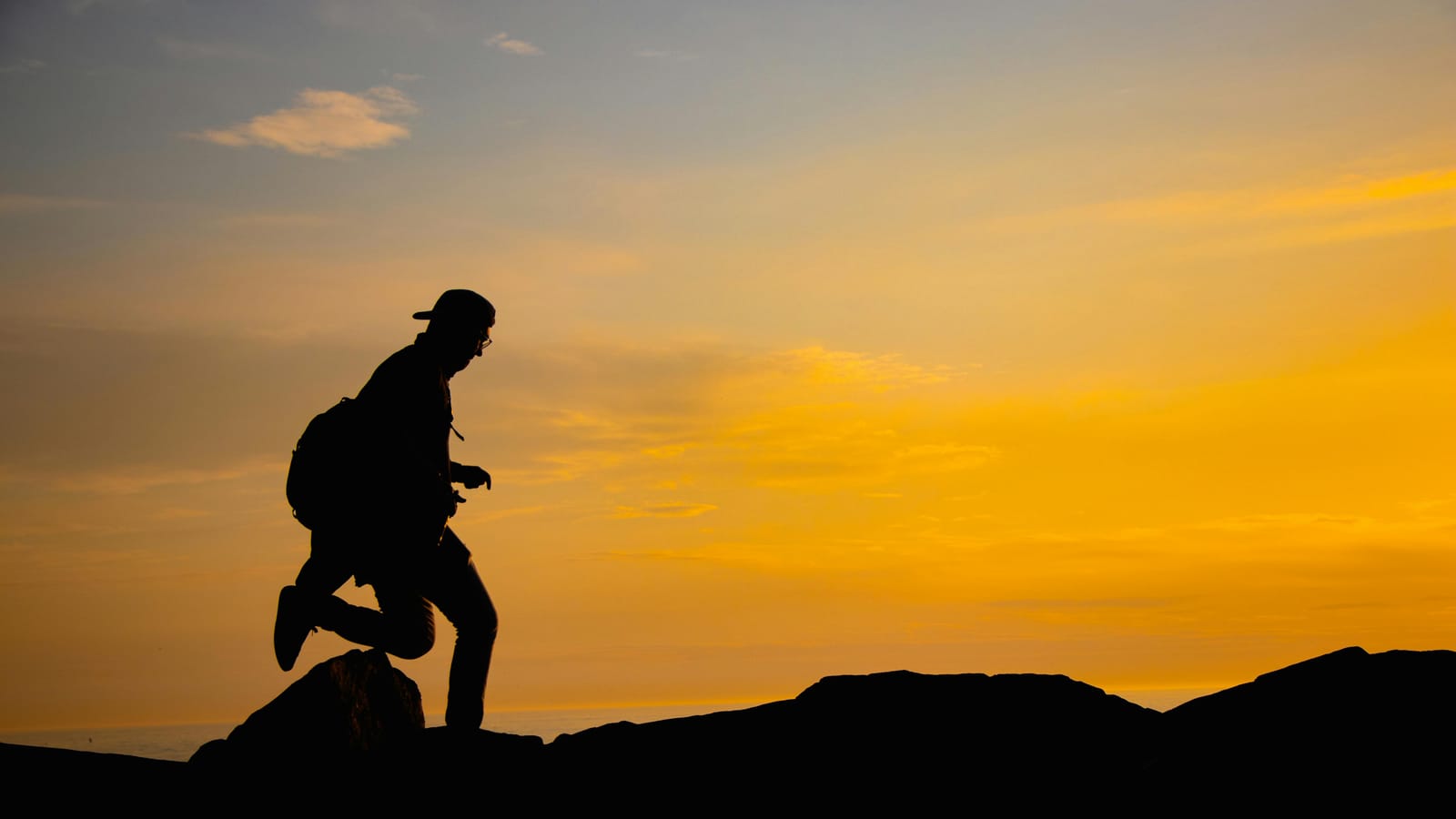 Silhouette of a person hiking on a mountain with a breathtaking sunrise sky background.