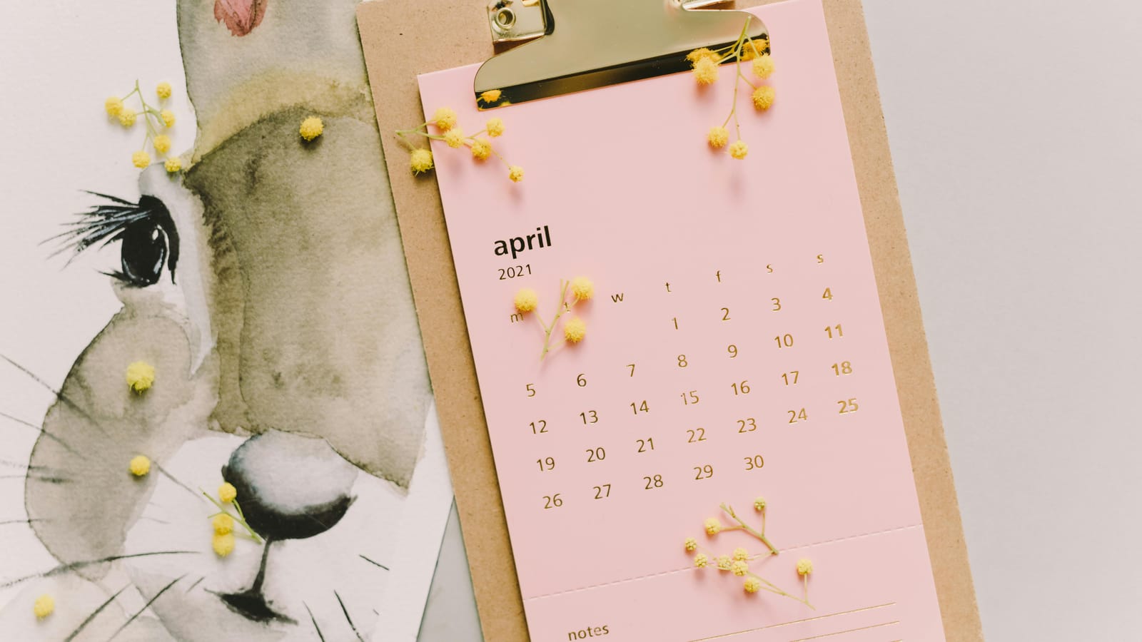 April 2021 calendar with watercolor bunny and mimosa flowers on clipboard.