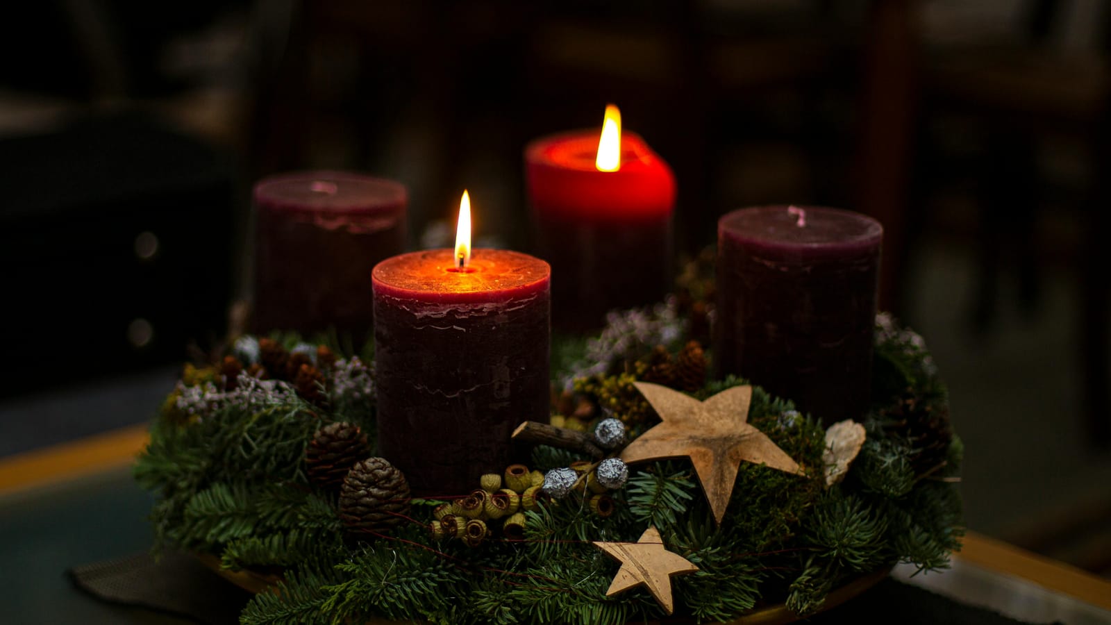 Lit candles on a decorative evergreen wreath with stars and pinecones create a cozy ambiance.